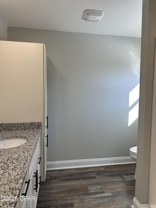 bathroom with wood finished floors, toilet, vanity, baseboards, and visible vents