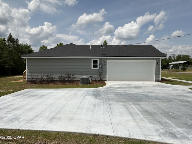 rear view of property with concrete driveway, central air condition unit, and an attached garage