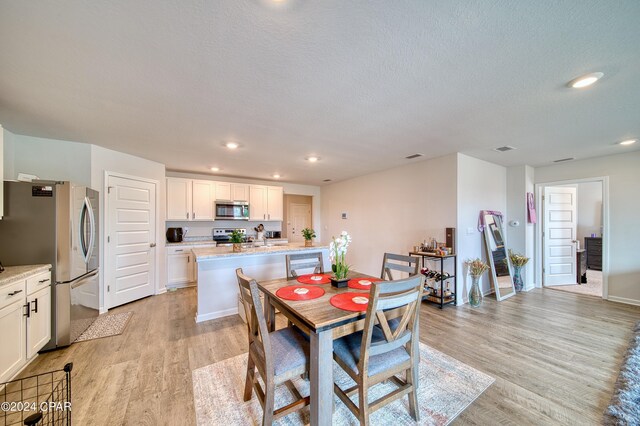 dining room with sink, a textured ceiling, and light hardwood / wood-style floors