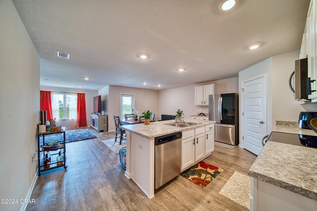 kitchen with appliances with stainless steel finishes, white cabinetry, an island with sink, and light wood-type flooring