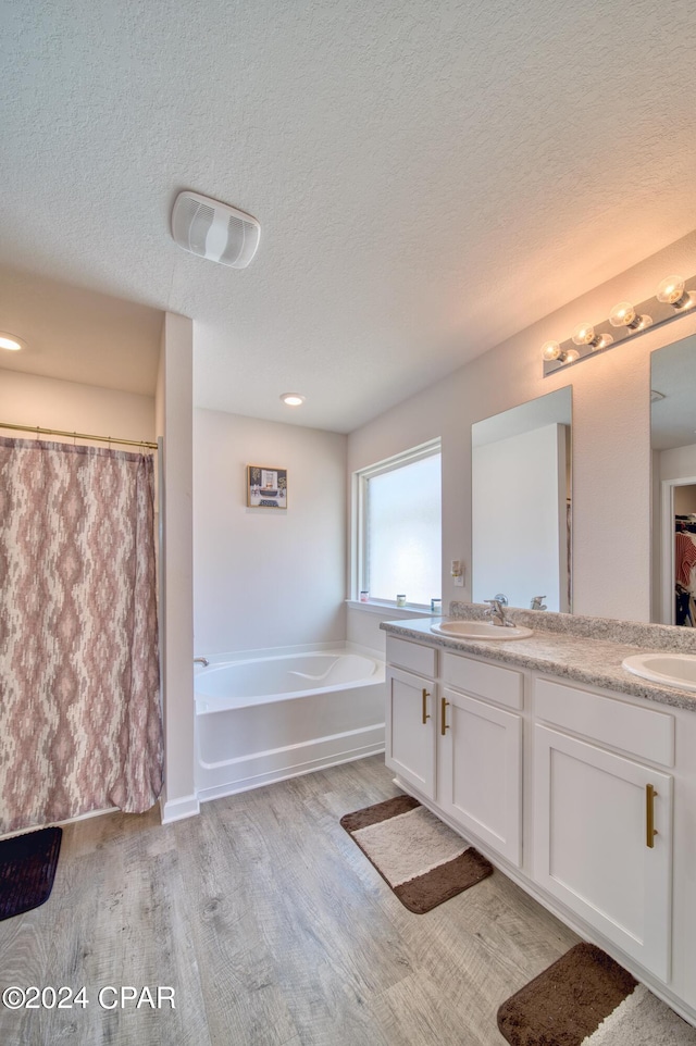 bathroom with a textured ceiling, double sink vanity, a washtub, and wood-type flooring