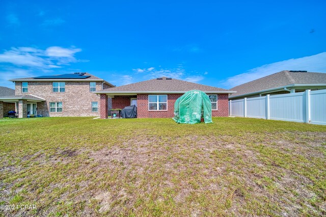 back of property with solar panels and a lawn