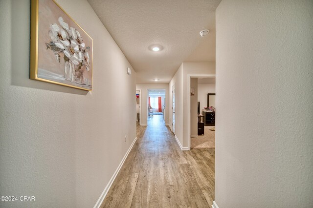 corridor with light hardwood / wood-style flooring and a textured ceiling