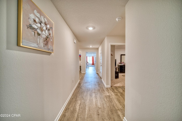 corridor with light hardwood / wood-style floors and a textured ceiling