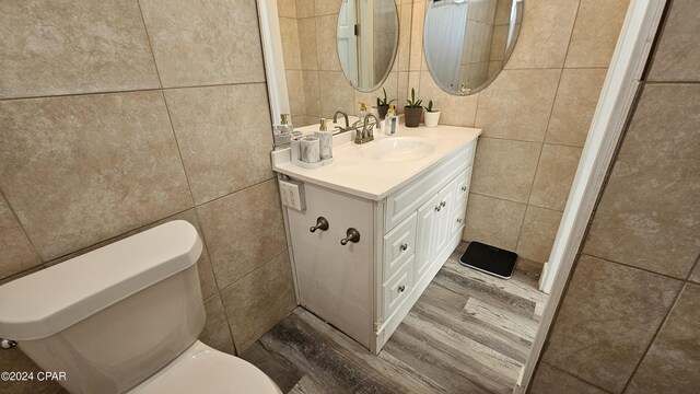 bathroom with hardwood / wood-style flooring, toilet, vanity, and tile walls