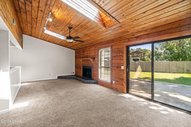 unfurnished living room with vaulted ceiling with skylight, ceiling fan, a fireplace, and carpet