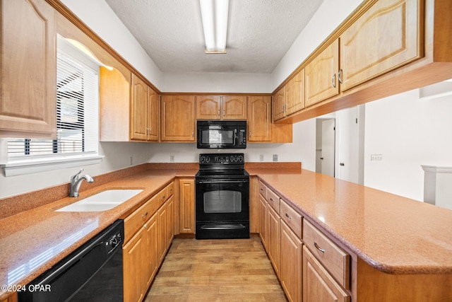 kitchen featuring light wood-type flooring, black appliances, a textured ceiling, and sink