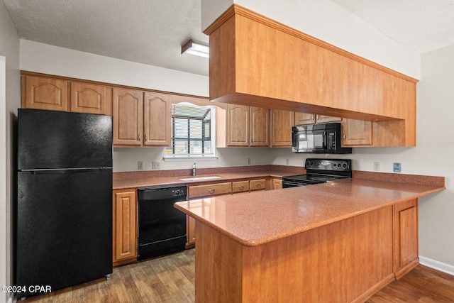 kitchen with black appliances, kitchen peninsula, sink, and light hardwood / wood-style flooring