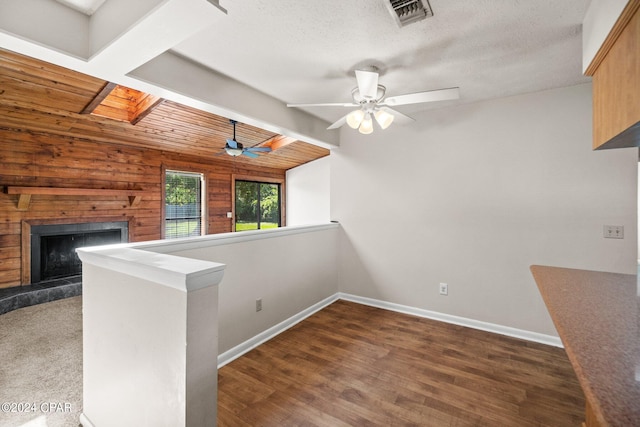 interior space with a tile fireplace, beamed ceiling, dark wood-type flooring, ceiling fan, and wooden ceiling