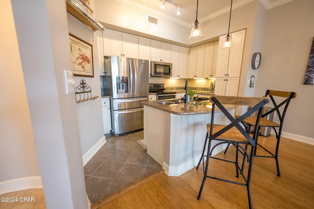 kitchen featuring appliances with stainless steel finishes, white cabinetry, rail lighting, hardwood / wood-style flooring, and hanging light fixtures