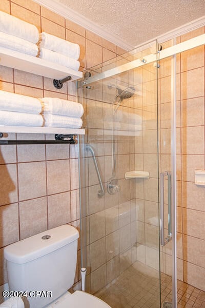 bathroom with a textured ceiling, a shower with shower door, tile walls, toilet, and crown molding