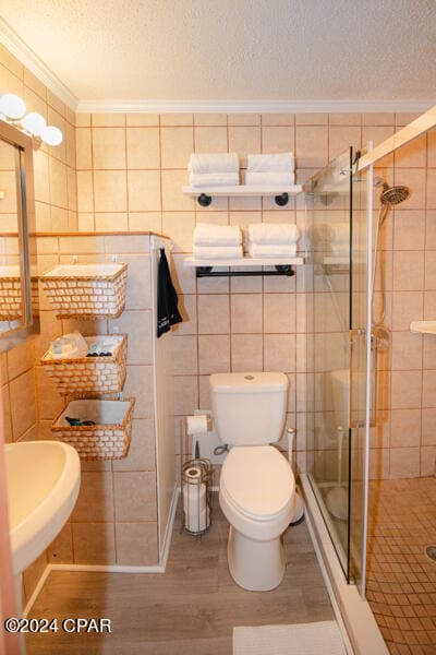 bathroom featuring toilet, a textured ceiling, tile walls, hardwood / wood-style flooring, and a shower with shower door