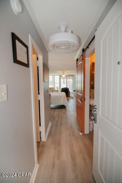 hall with ornamental molding, a barn door, and light hardwood / wood-style floors