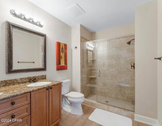 bathroom with wood-type flooring, a shower with door, vanity, and toilet