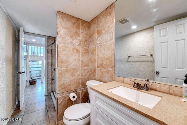 bathroom with tile patterned floors, toilet, tile walls, vanity, and walk in shower