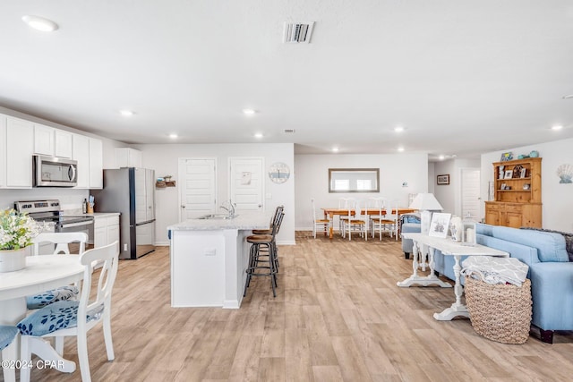 kitchen featuring stainless steel appliances, light hardwood / wood-style flooring, white cabinetry, sink, and a kitchen breakfast bar