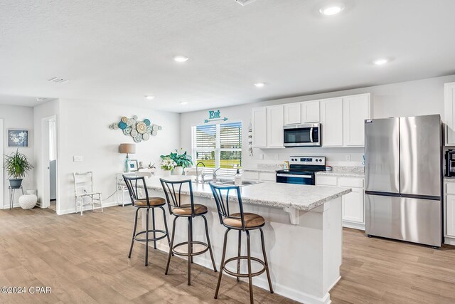 kitchen with a kitchen bar, a center island, light hardwood / wood-style floors, white cabinetry, and stainless steel appliances