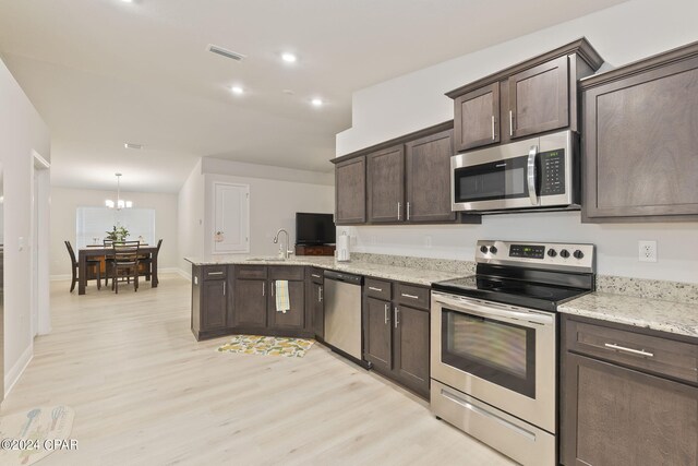 kitchen with an inviting chandelier, light stone countertops, dark brown cabinets, appliances with stainless steel finishes, and light wood-type flooring