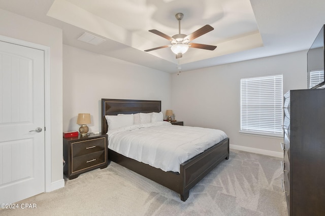 bedroom with light colored carpet, ceiling fan, a raised ceiling, and multiple windows