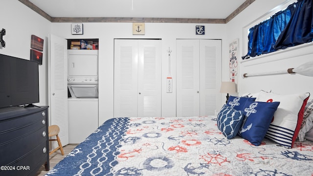 bedroom with crown molding, stacked washer and clothes dryer, wood-type flooring, and two closets