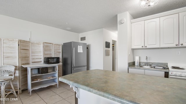 kitchen with light tile patterned flooring, white cabinetry, sink, stainless steel fridge, and a textured ceiling