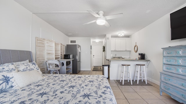 bedroom with light tile patterned floors, a textured ceiling, stainless steel fridge, and ceiling fan