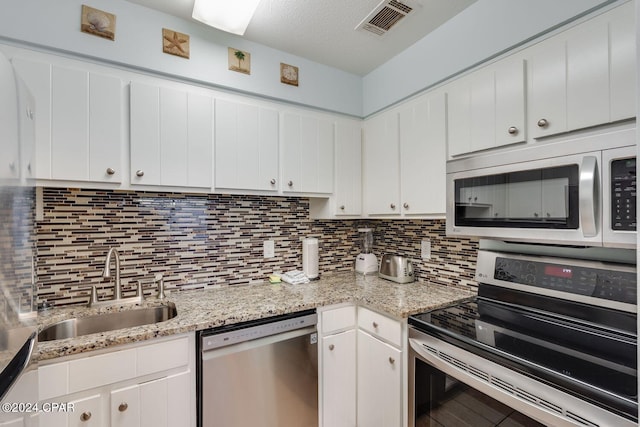 kitchen with stainless steel appliances, tasteful backsplash, a sink, and white cabinetry