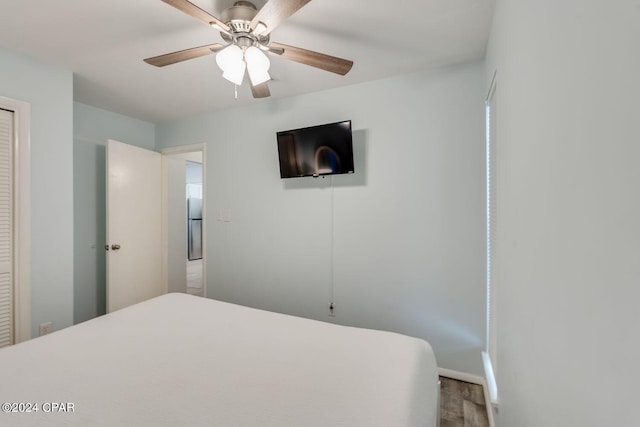 bedroom featuring baseboards, ceiling fan, wood finished floors, freestanding refrigerator, and a closet