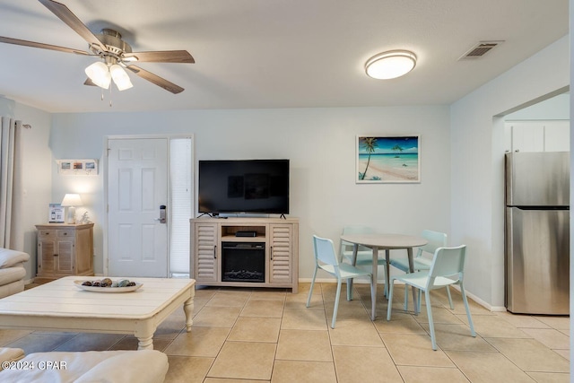 living room featuring light tile patterned flooring, a fireplace, visible vents, a ceiling fan, and baseboards