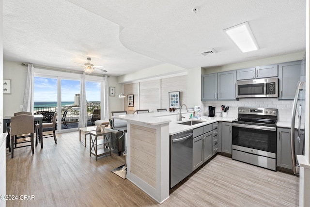 kitchen with stainless steel appliances, kitchen peninsula, sink, ceiling fan, and light hardwood / wood-style floors