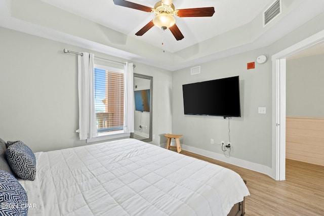 bedroom featuring light wood-type flooring, ceiling fan, and a raised ceiling