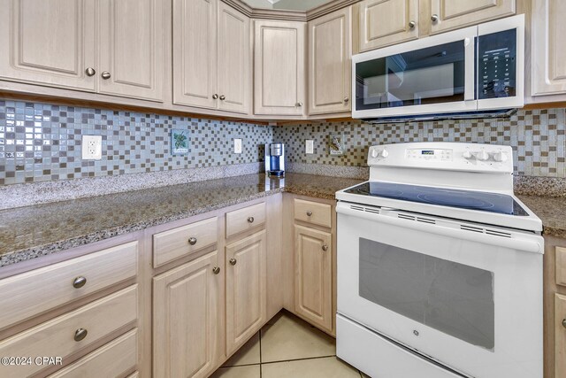 kitchen with light tile patterned flooring, decorative backsplash, light brown cabinets, light stone counters, and white range with electric stovetop