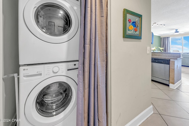 washroom with stacked washer and dryer, a textured ceiling, laundry area, light tile patterned floors, and baseboards