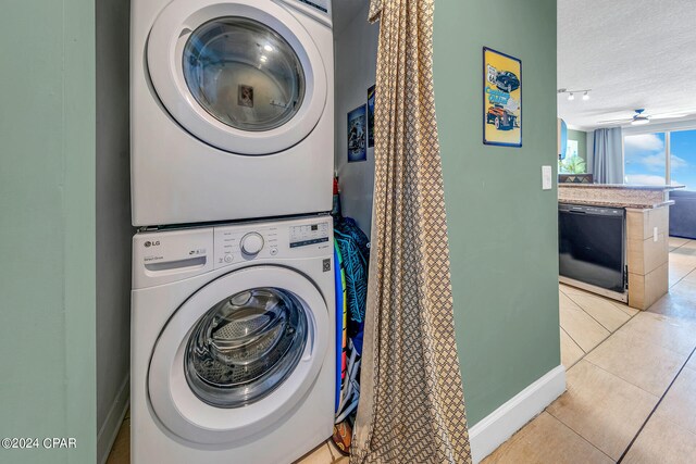 laundry area with stacked washing maching and dryer, light tile patterned floors, laundry area, and a textured ceiling