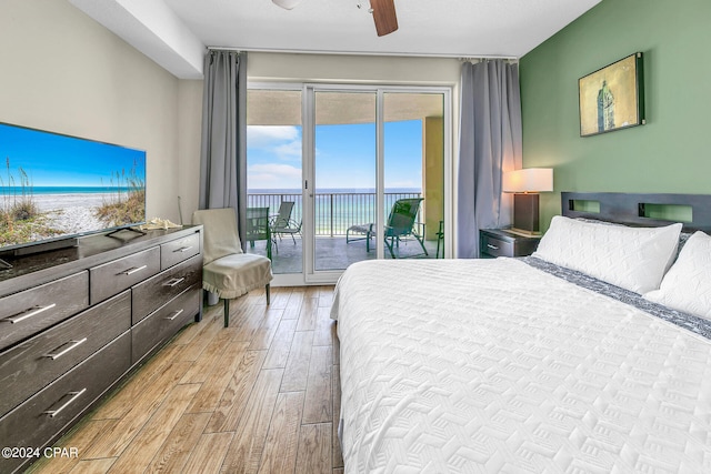 bedroom with light wood-type flooring, access to outside, a water view, and a ceiling fan