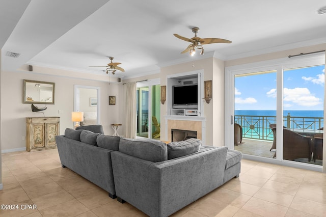 living room with a tiled fireplace, ceiling fan, light tile patterned floors, and crown molding