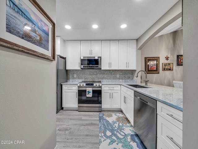 kitchen featuring light hardwood / wood-style floors, tasteful backsplash, sink, white cabinetry, and stainless steel appliances