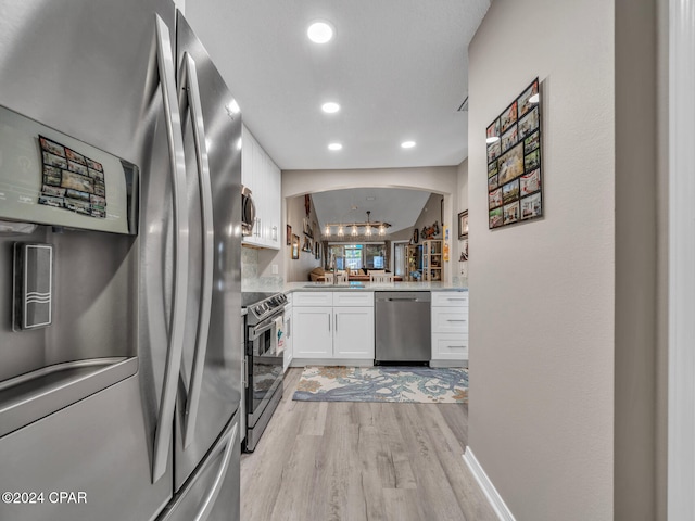 kitchen with appliances with stainless steel finishes, light hardwood / wood-style floors, white cabinetry, kitchen peninsula, and a notable chandelier