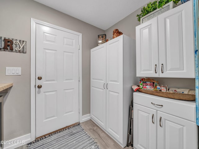 clothes washing area featuring light wood-type flooring, a textured ceiling, and cabinets