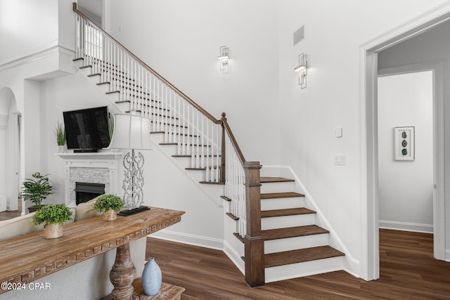 stairway with a fireplace, hardwood / wood-style floors, and a towering ceiling