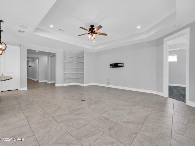 unfurnished room with ceiling fan, built in features, and a raised ceiling