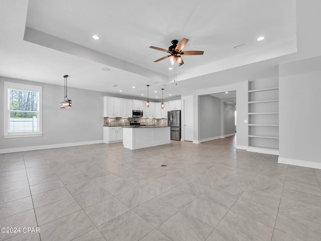 unfurnished living room featuring ceiling fan, built in shelves, light tile patterned floors, and a raised ceiling