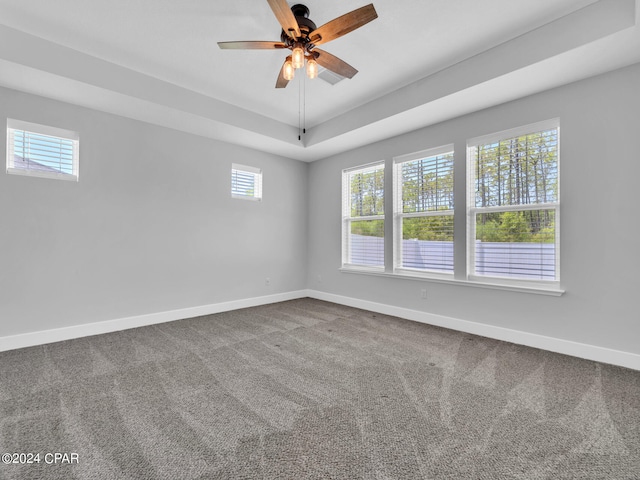 carpeted empty room featuring ceiling fan, a raised ceiling, and plenty of natural light