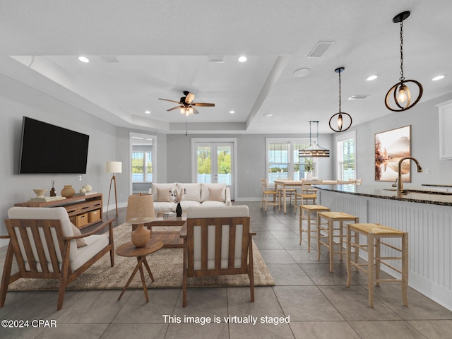 living room with french doors, a tray ceiling, sink, light tile patterned floors, and ceiling fan