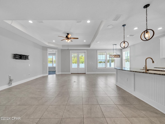 unfurnished living room with french doors, a tray ceiling, sink, light tile patterned flooring, and ceiling fan