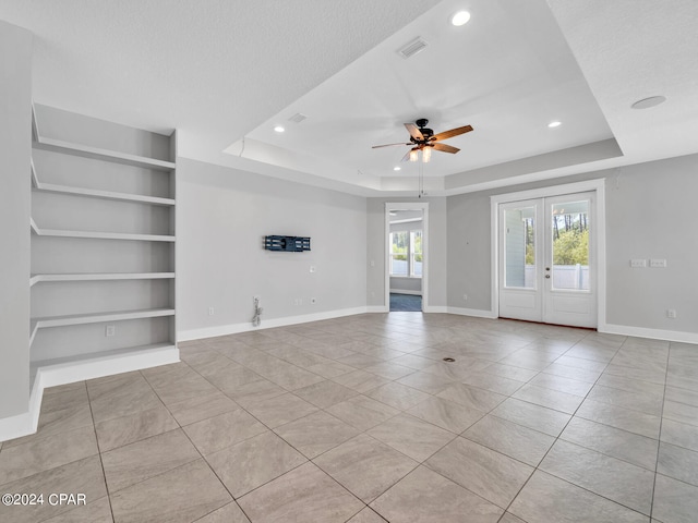 unfurnished living room with ceiling fan, a textured ceiling, built in features, and a tray ceiling