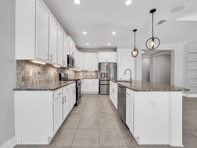 kitchen featuring a kitchen island with sink, stainless steel appliances, dark stone counters, sink, and white cabinets