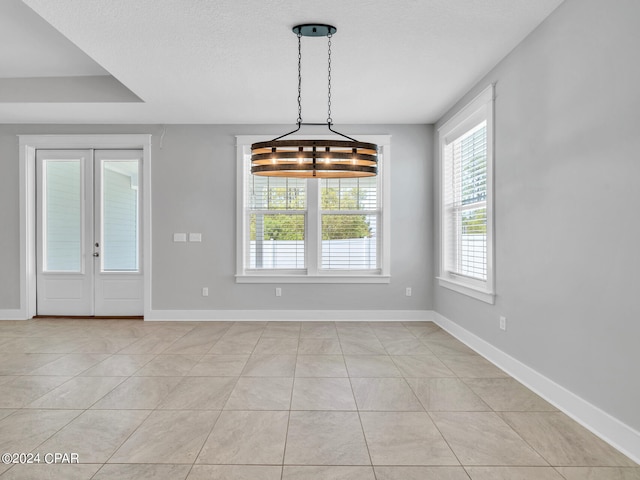 unfurnished dining area featuring french doors, a textured ceiling, a chandelier, and light tile patterned floors