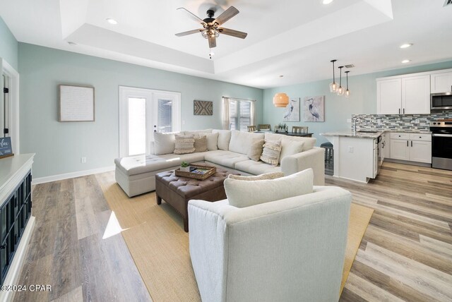 living room with a tray ceiling, ceiling fan, light hardwood / wood-style floors, and sink