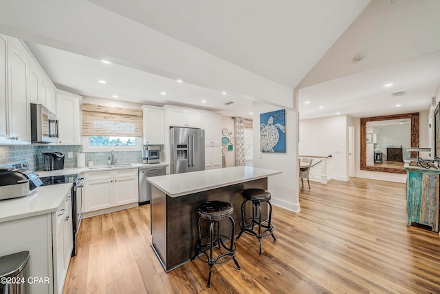 kitchen featuring light hardwood / wood-style floors, a center island, white cabinets, lofted ceiling, and stainless steel appliances